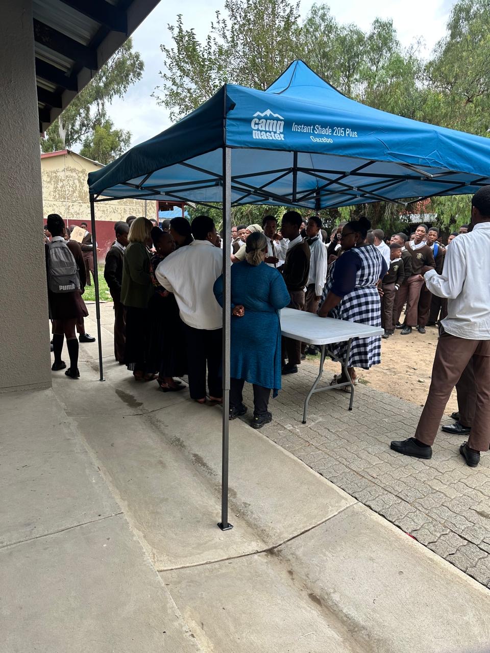 Learners queueing at a gazebo during an open air school outreach