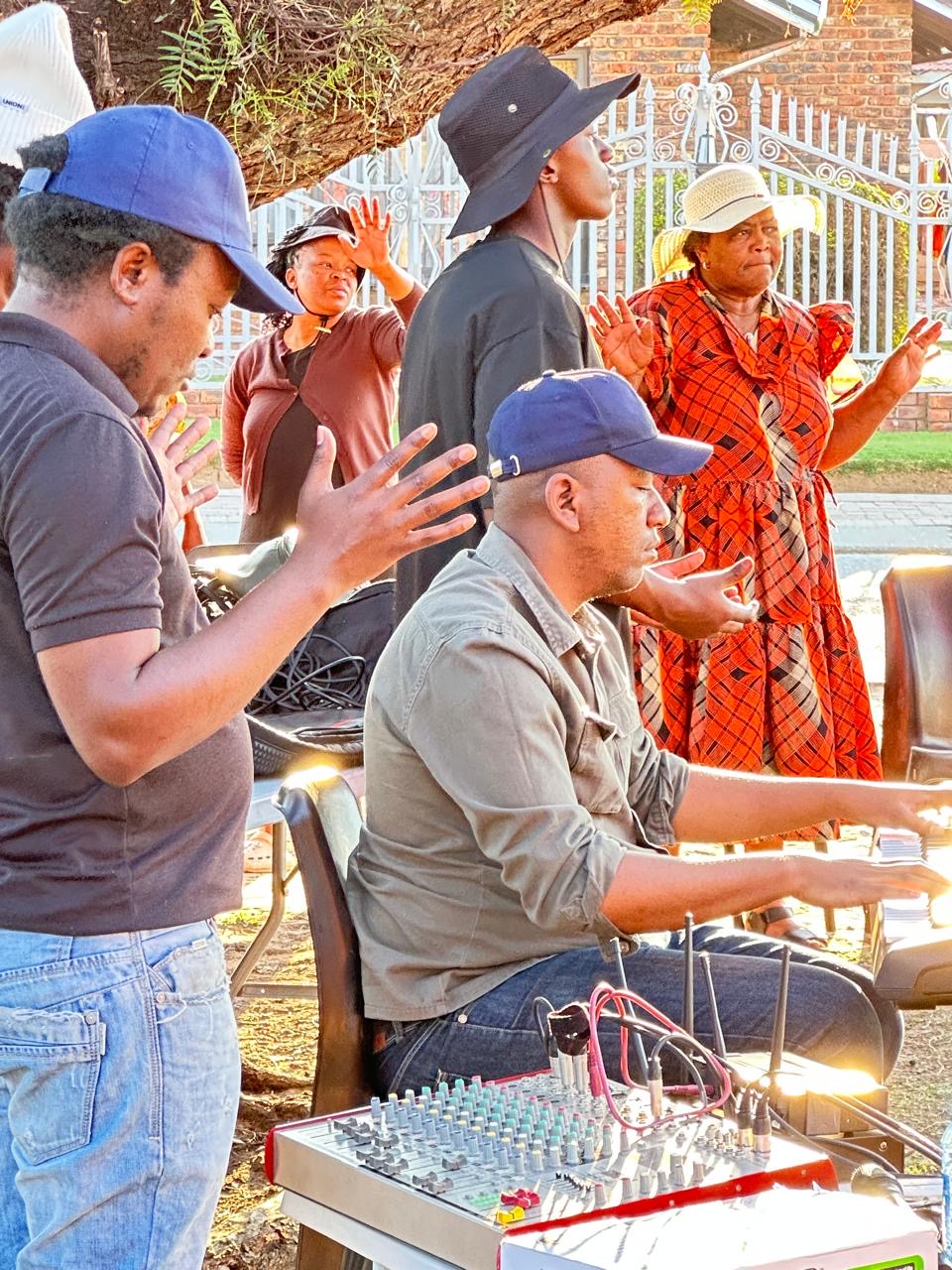 Worshippers with raised hands beside a keyboard player outdoors