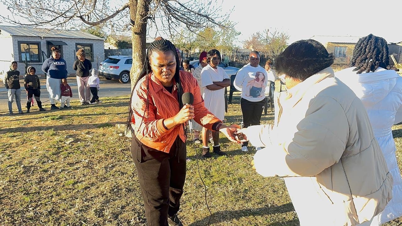 A woman praying with a community member during an outdoor gathering
