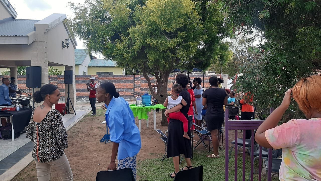 Community members gathered under trees in a yard during an open air fellowship