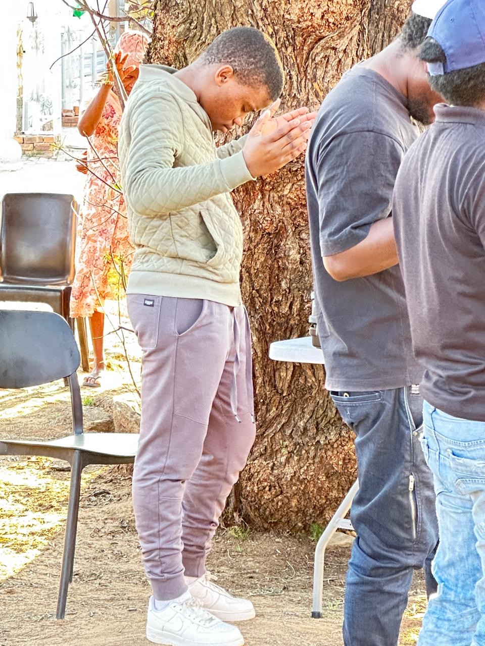 A young man praying with hands clasped under a tree