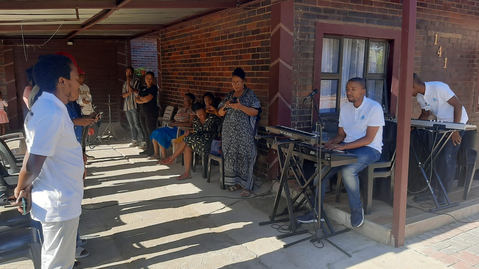 Worship team playing keyboards on a stoep while the congregation stands and sings
