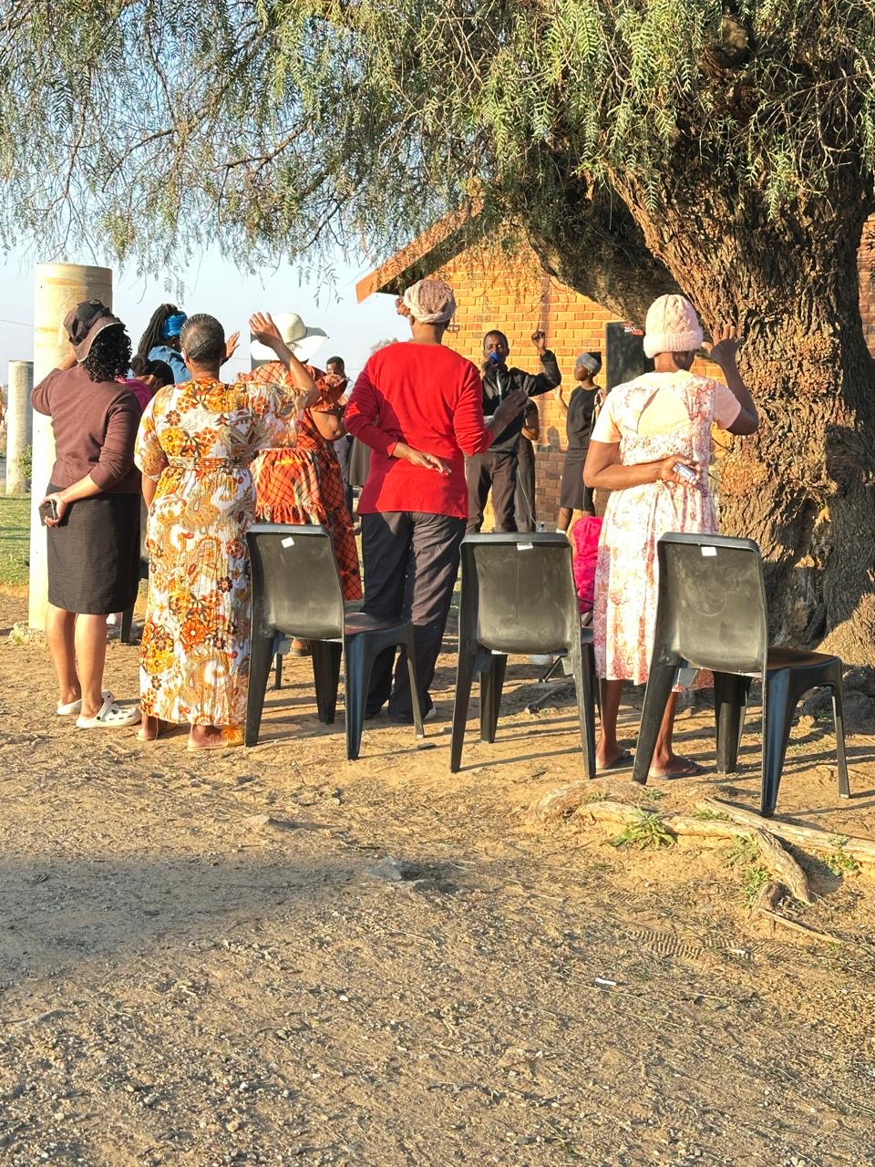 Community members standing and worshipping in the late afternoon sun