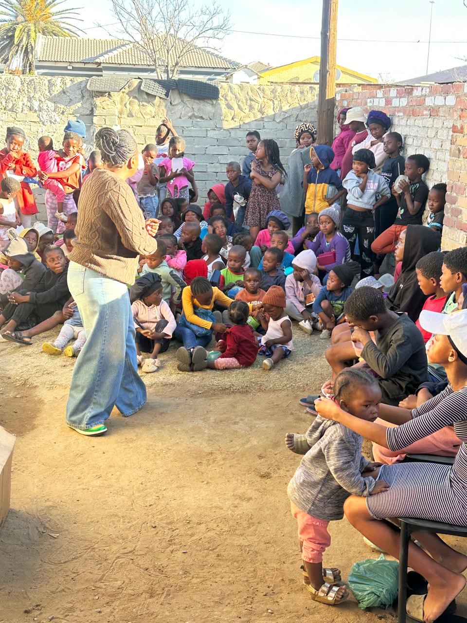 Children seated on the ground listening during a community outreach